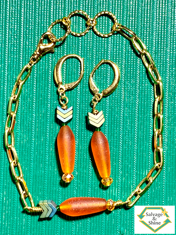 wearable art earrings and bracelet set with gold metals and with beaded carrot charms (an orange root and green stem and leaves). The bracelet is a paperclip chain.