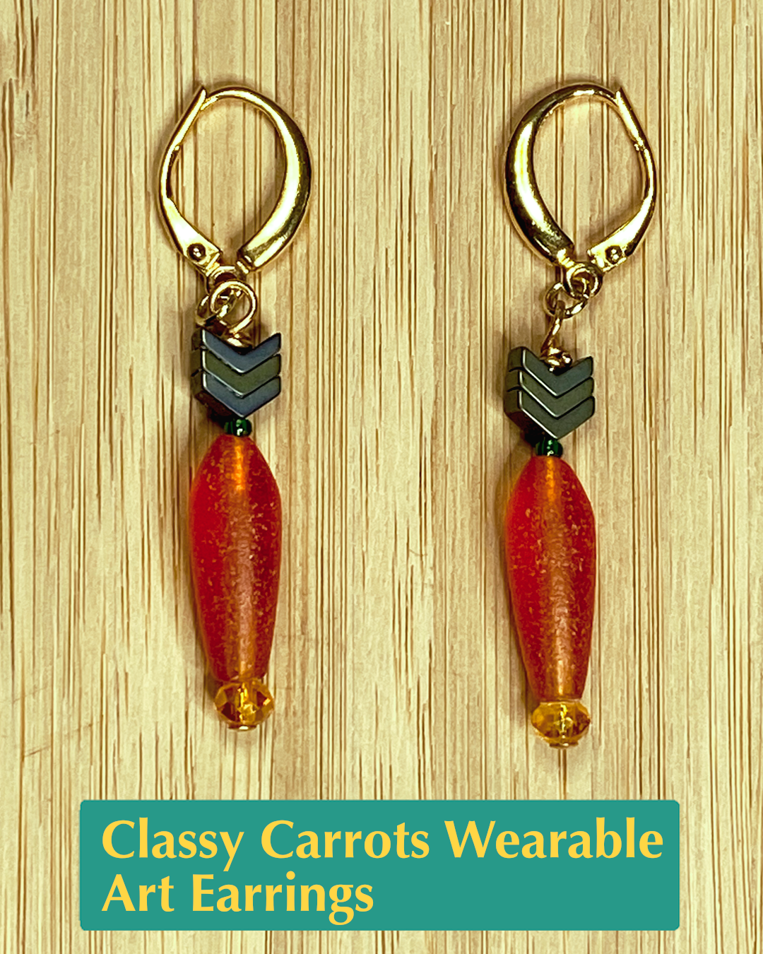 wearable art earrings shaped like carrots that have an orange root, a green stem and leaves, and gold metals. 